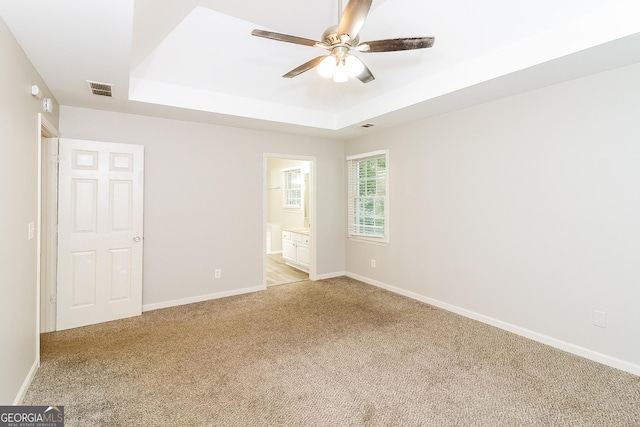 unfurnished bedroom with connected bathroom, light colored carpet, a raised ceiling, and ceiling fan