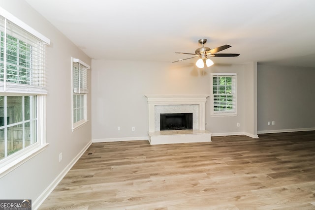 unfurnished living room with ceiling fan, a premium fireplace, and light hardwood / wood-style flooring