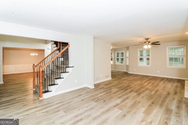 unfurnished living room featuring ceiling fan with notable chandelier, light hardwood / wood-style floors, and a wealth of natural light