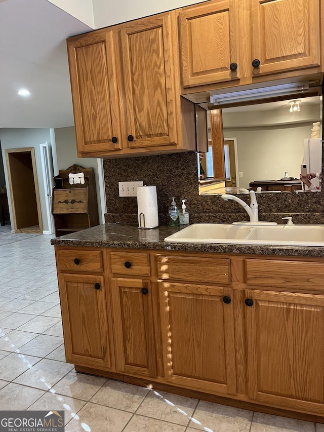 kitchen with light tile patterned floors, dark stone countertops, sink, and backsplash