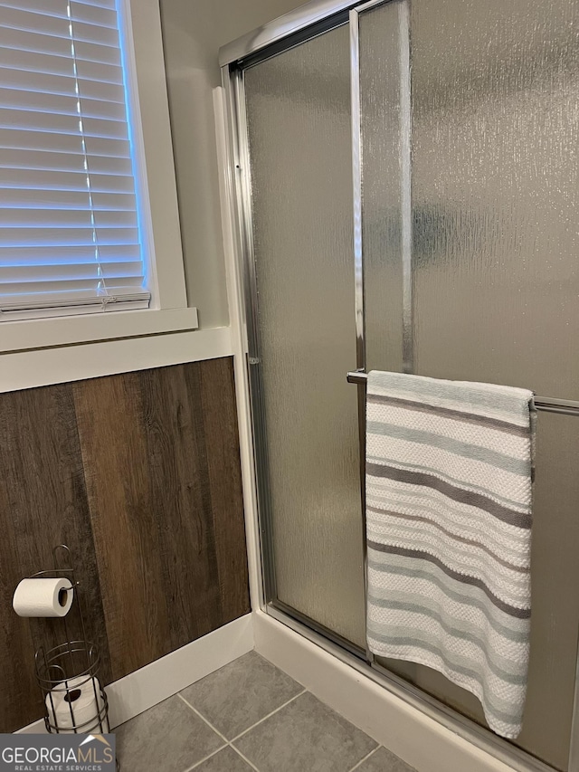 bathroom with tile patterned flooring, walk in shower, and wood walls