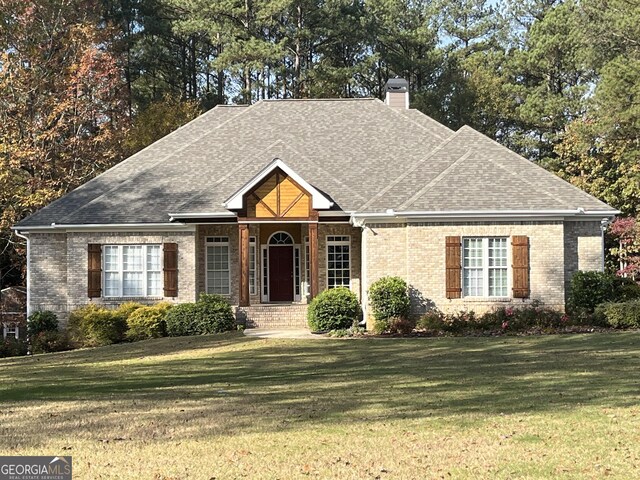 view of front of property featuring brick siding, a front lawn, a chimney, and a shingled roof