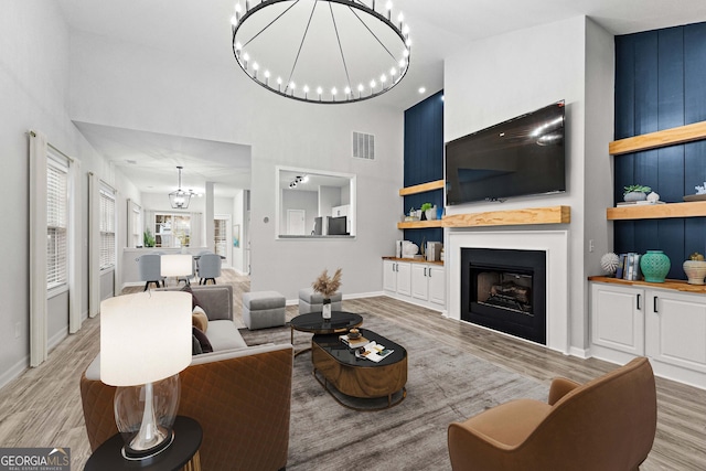 living room with a towering ceiling, light hardwood / wood-style floors, and an inviting chandelier