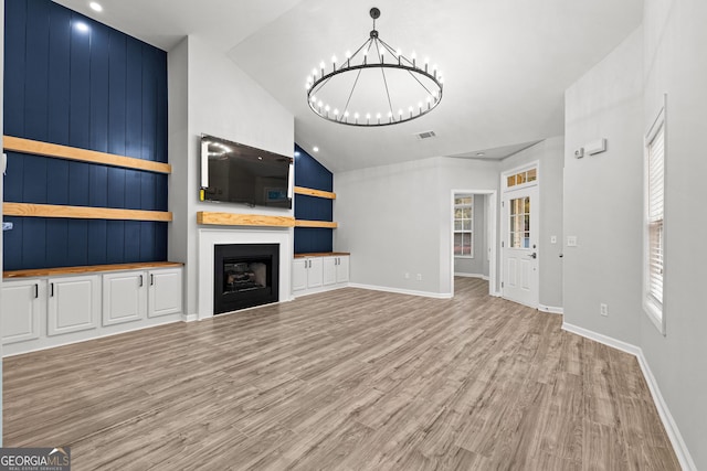 unfurnished living room featuring high vaulted ceiling, wooden walls, light hardwood / wood-style flooring, a fireplace, and a notable chandelier