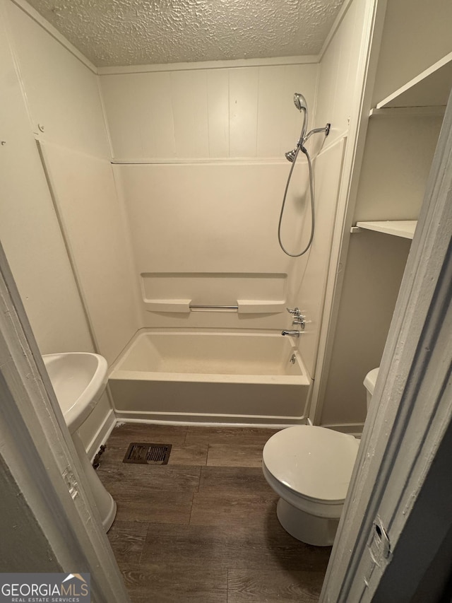 bathroom featuring hardwood / wood-style flooring, toilet, washtub / shower combination, and a textured ceiling