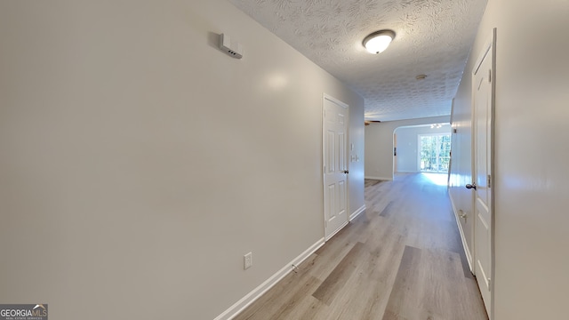 hallway with a textured ceiling and light hardwood / wood-style floors