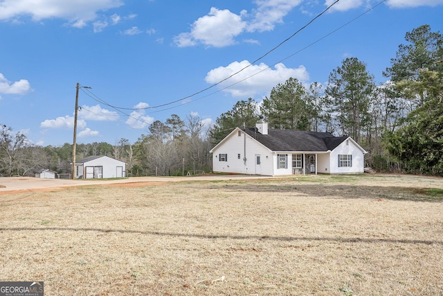 exterior space featuring a detached garage, a chimney, a front lawn, and an outdoor structure