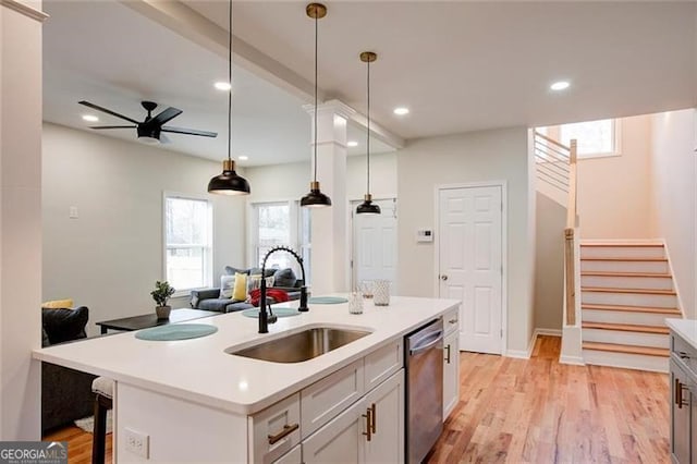 kitchen with stainless steel dishwasher, ceiling fan, sink, a center island with sink, and white cabinets