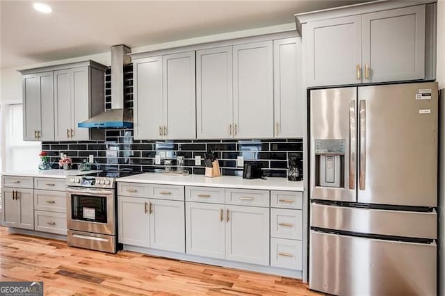 kitchen featuring light wood-type flooring, stainless steel appliances, tasteful backsplash, and wall chimney range hood