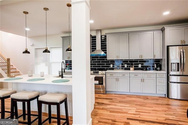 kitchen featuring pendant lighting, wall chimney range hood, sink, gray cabinets, and appliances with stainless steel finishes