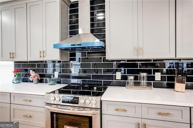 kitchen featuring wall chimney exhaust hood, gray cabinets, decorative backsplash, and stainless steel range