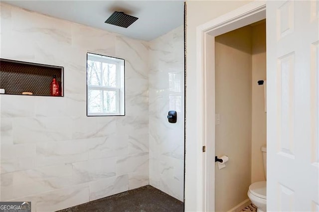 bathroom with a tile shower and toilet