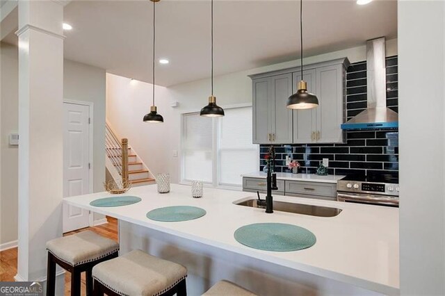 kitchen with gray cabinetry, wall chimney exhaust hood, hanging light fixtures, tasteful backsplash, and range