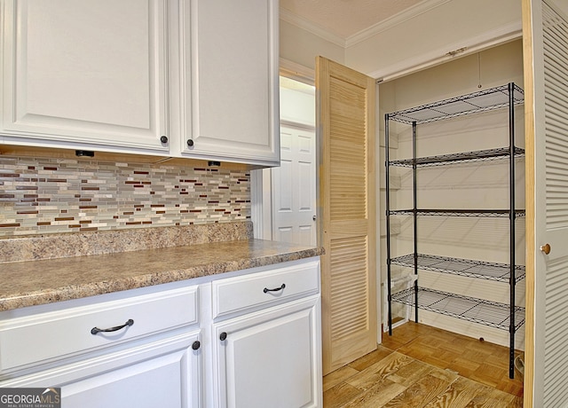 interior space with tasteful backsplash, white cabinetry, ornamental molding, and light parquet flooring