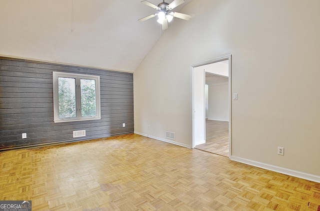 empty room with ceiling fan, high vaulted ceiling, light parquet floors, and wood walls