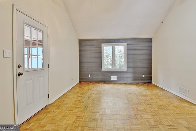 entrance foyer featuring light parquet floors, lofted ceiling, and wood walls