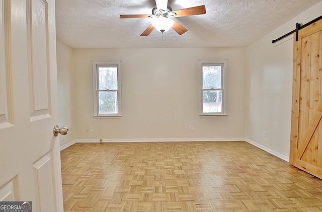 empty room featuring light parquet flooring, a barn door, a textured ceiling, and a wealth of natural light