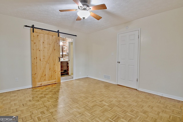 empty room with light parquet floors, ceiling fan, a barn door, and a textured ceiling