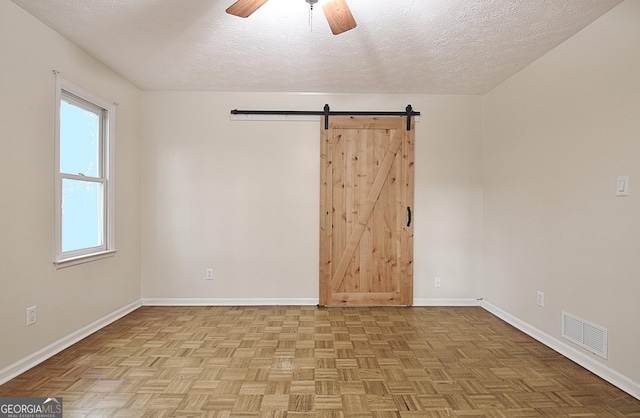 unfurnished room featuring light parquet flooring, a barn door, ceiling fan, and a textured ceiling