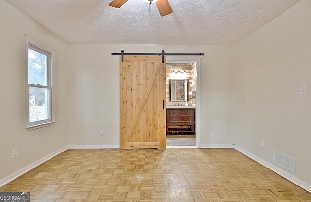 unfurnished room with ceiling fan, light parquet flooring, a barn door, and a textured ceiling