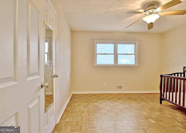 bedroom with a nursery area, ceiling fan, light parquet flooring, and a textured ceiling