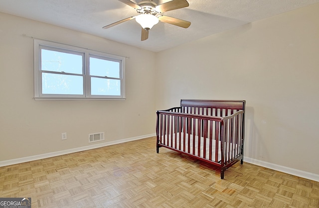 bedroom with a crib, light parquet flooring, ceiling fan, and a textured ceiling