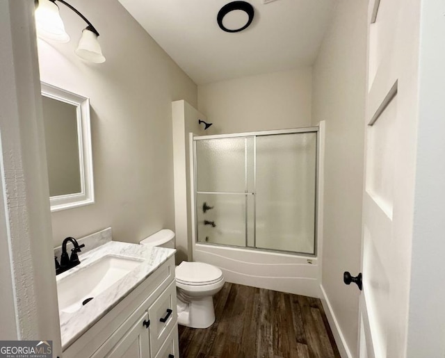 full bathroom featuring hardwood / wood-style floors, toilet, combined bath / shower with glass door, and vanity