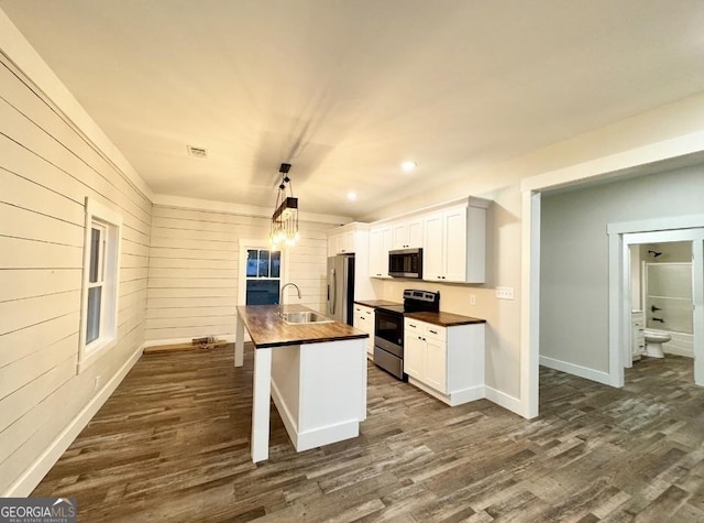 kitchen with stainless steel appliances, dark wood-type flooring, a center island with sink, white cabinets, and hanging light fixtures