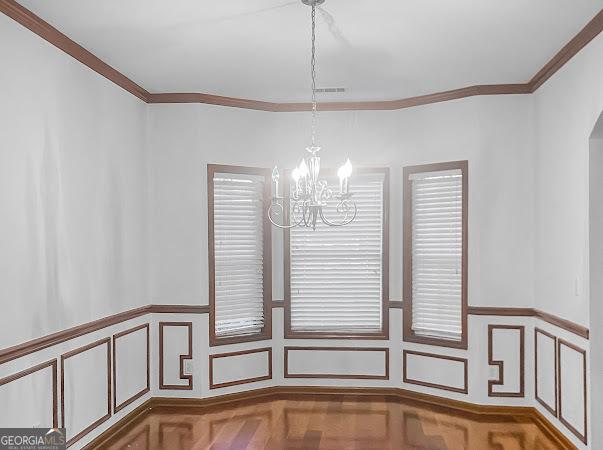 unfurnished dining area with an inviting chandelier, parquet floors, and ornamental molding