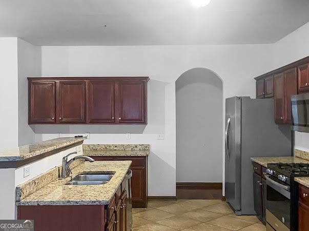 kitchen with light stone countertops, an island with sink, stainless steel appliances, and sink