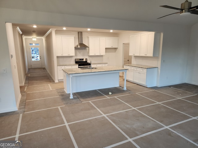 kitchen featuring a center island with sink, wall chimney range hood, light stone countertops, stainless steel range oven, and white cabinetry