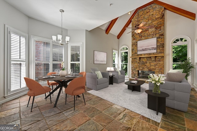 dining room featuring beam ceiling, ceiling fan with notable chandelier, high vaulted ceiling, and a stone fireplace