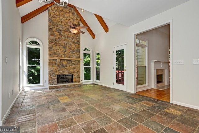 unfurnished living room featuring ceiling fan, beam ceiling, a stone fireplace, and high vaulted ceiling