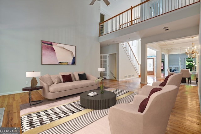 living room featuring ceiling fan with notable chandelier, light hardwood / wood-style floors, and a towering ceiling