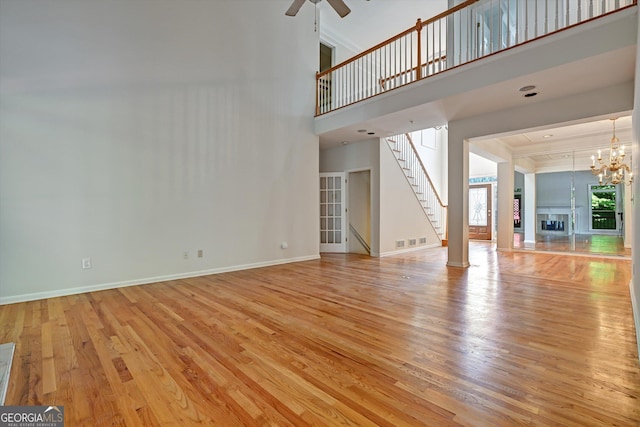 unfurnished living room with ceiling fan with notable chandelier, light wood-type flooring, and a towering ceiling