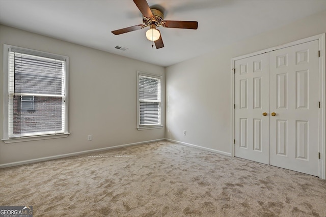 unfurnished bedroom featuring ceiling fan, a closet, light carpet, and multiple windows