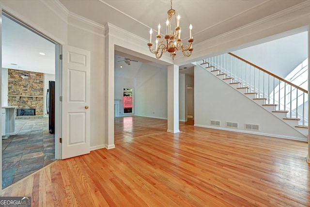 interior space featuring a stone fireplace, crown molding, ceiling fan with notable chandelier, and hardwood / wood-style flooring