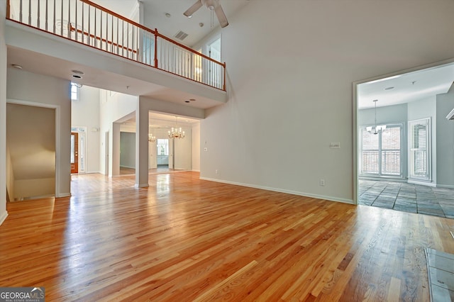 unfurnished living room featuring ceiling fan with notable chandelier, a towering ceiling, and light hardwood / wood-style flooring