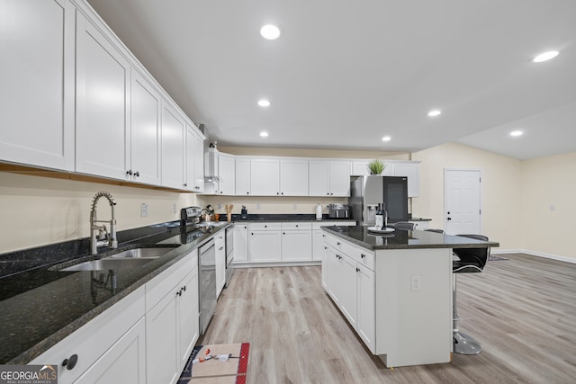 kitchen featuring a breakfast bar, dark stone counters, sink, appliances with stainless steel finishes, and white cabinetry