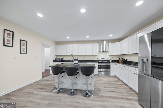 kitchen featuring white cabinets, appliances with stainless steel finishes, light hardwood / wood-style flooring, and wall chimney range hood