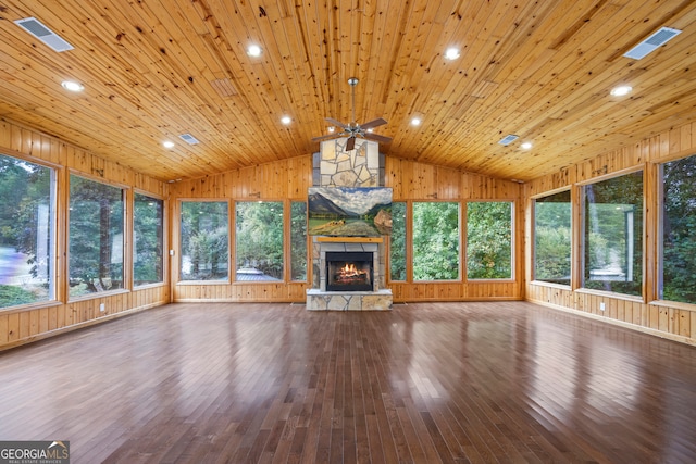 unfurnished living room with a healthy amount of sunlight, wooden walls, wood-type flooring, and vaulted ceiling