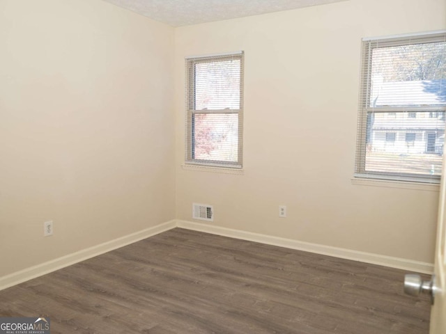 empty room featuring a healthy amount of sunlight, dark hardwood / wood-style flooring, and a textured ceiling