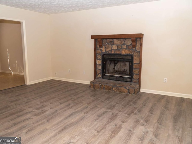 unfurnished living room featuring hardwood / wood-style floors, a stone fireplace, and a textured ceiling