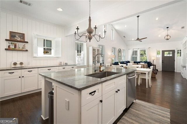 kitchen with dishwasher, dark stone counters, ceiling fan with notable chandelier, sink, and vaulted ceiling