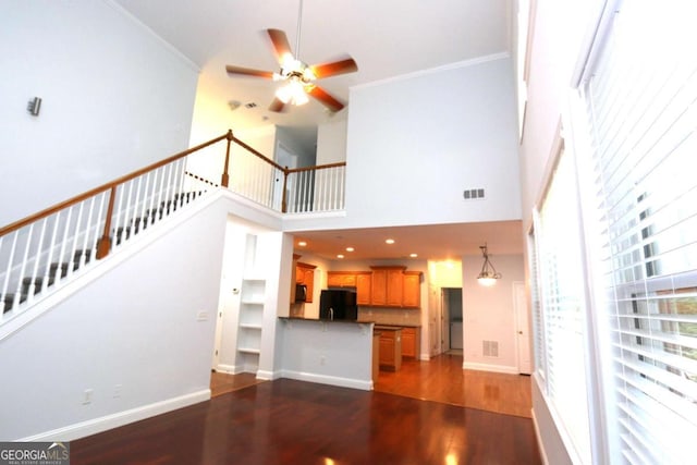 unfurnished living room with dark wood-type flooring, ceiling fan, a towering ceiling, and crown molding