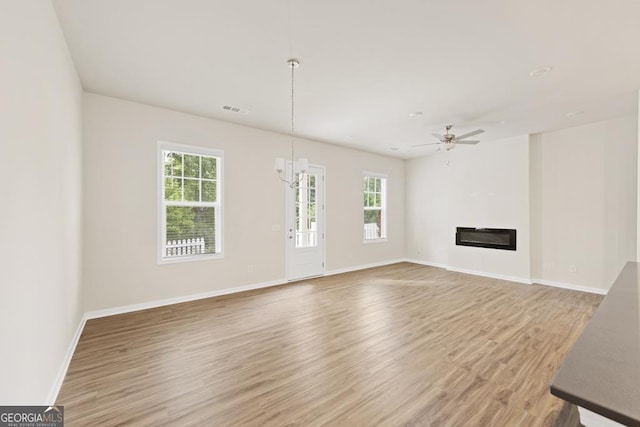 unfurnished living room featuring hardwood / wood-style floors and ceiling fan with notable chandelier