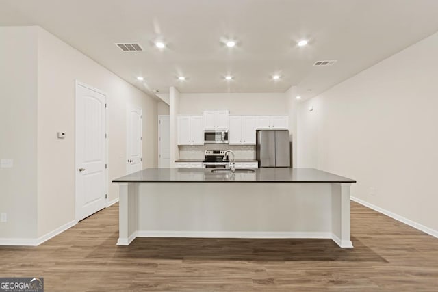 kitchen featuring white cabinets, a large island with sink, stainless steel appliances, and wood-type flooring