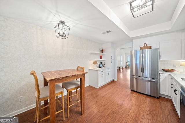 kitchen with stainless steel refrigerator, hanging light fixtures, light hardwood / wood-style flooring, backsplash, and white cabinets