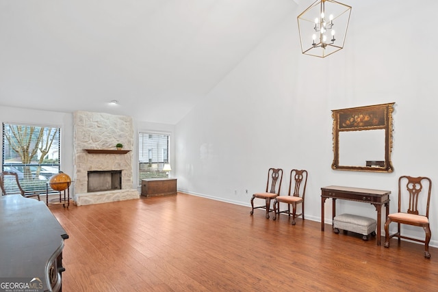 sitting room with an inviting chandelier, hardwood / wood-style flooring, a stone fireplace, and plenty of natural light