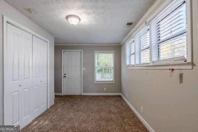 unfurnished bedroom featuring a textured ceiling, carpet floors, multiple windows, and ornamental molding